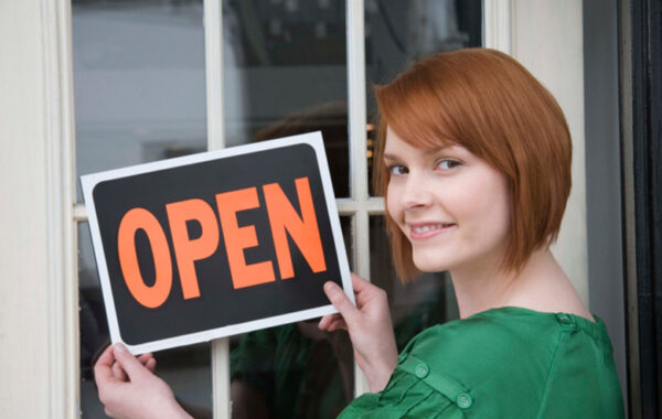 Smiling shop owner holding an 'Open' sign in a storefront doorway
