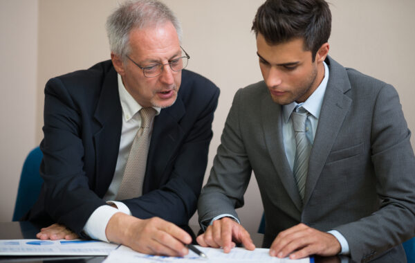 Senior business owner reviewing documents with a younger colleague, representing a business ownership transition